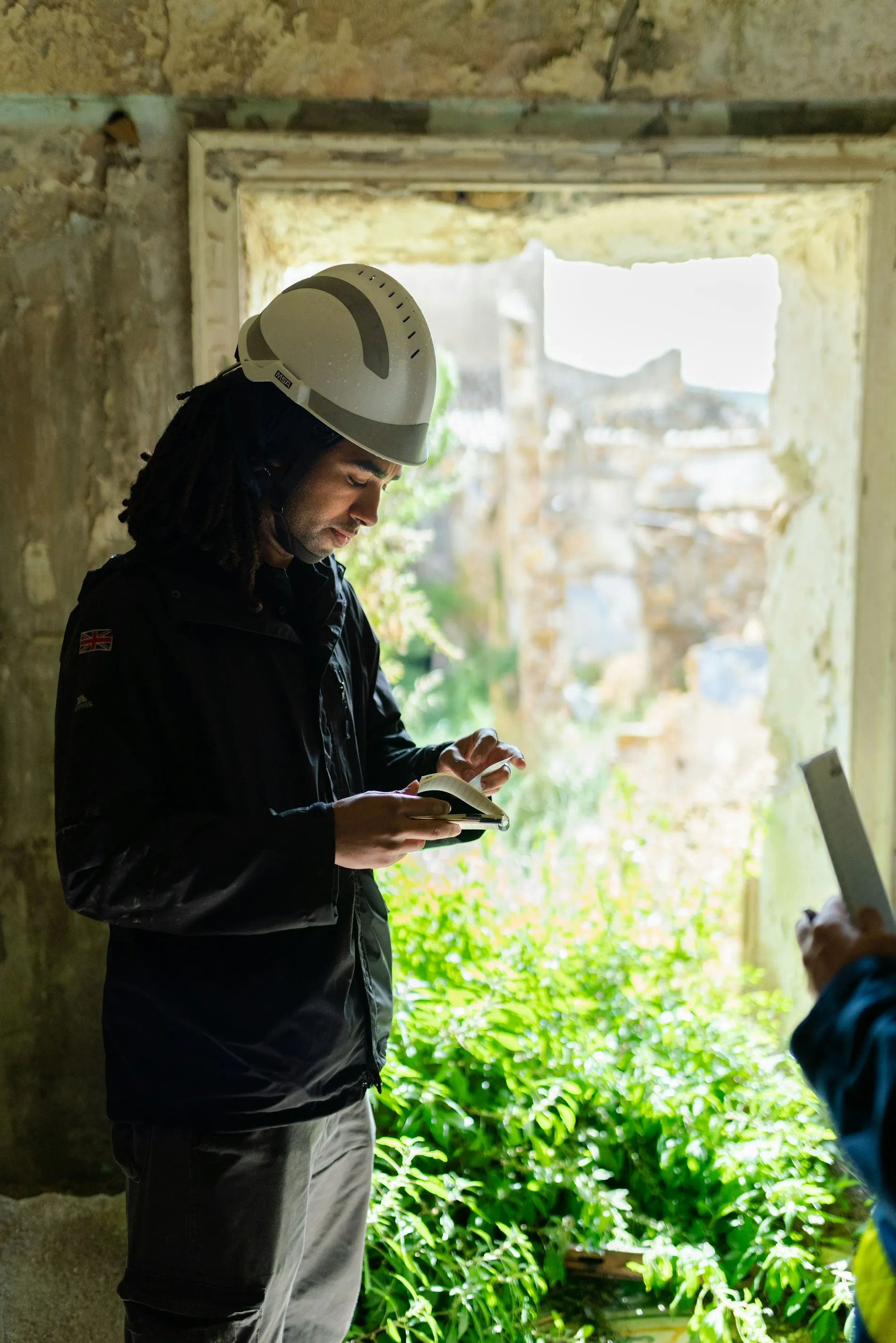A woman in a white hard hat checking her phone in a bright doorway on site