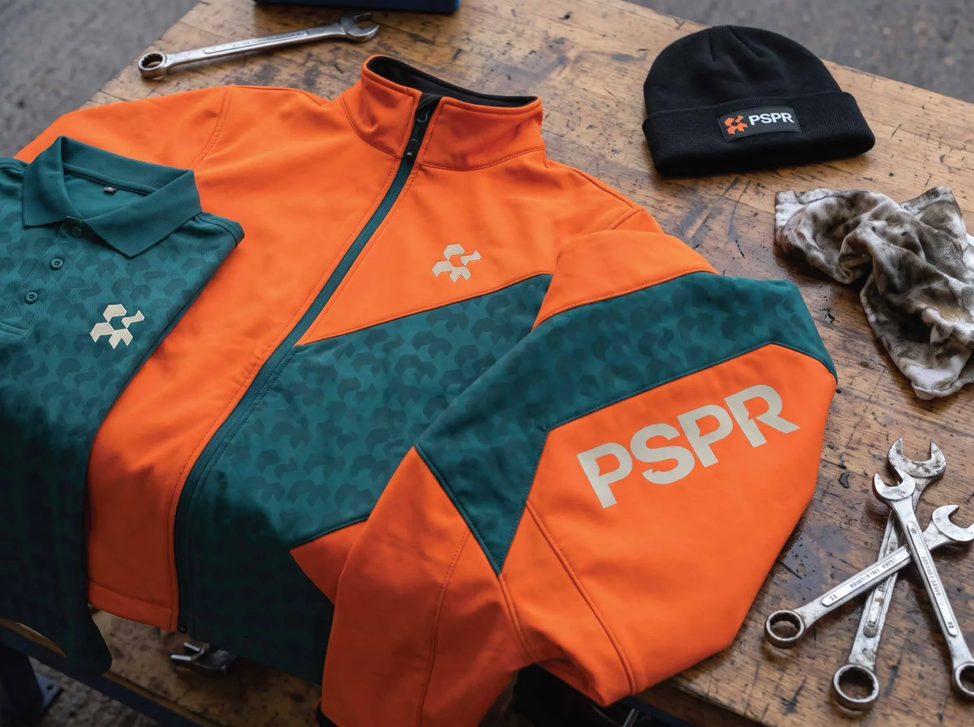 PSPR branded softshell jacket, polo and beanie on a workbench