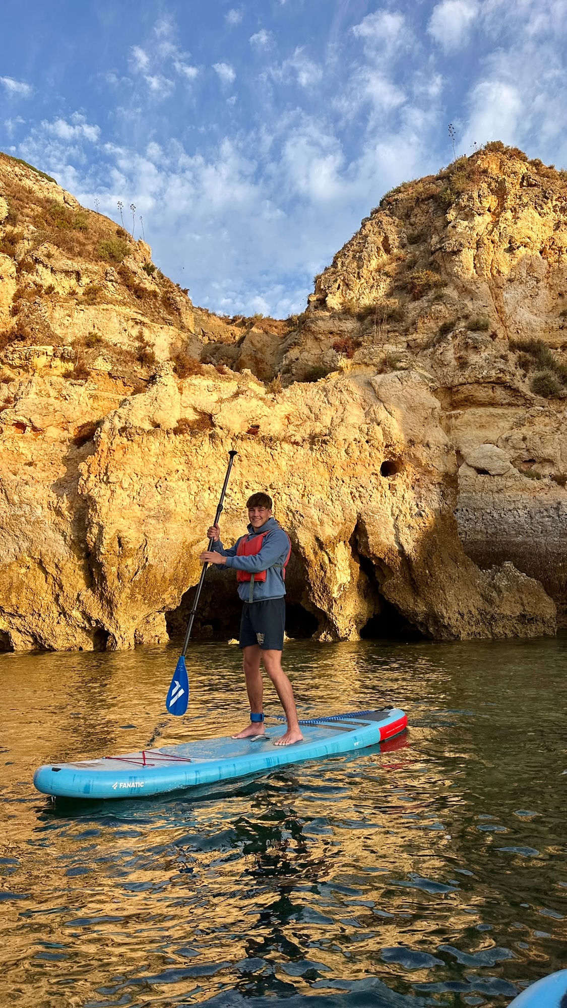 Jack Paterson standing on a paddleboard beneath golden sea cliffs